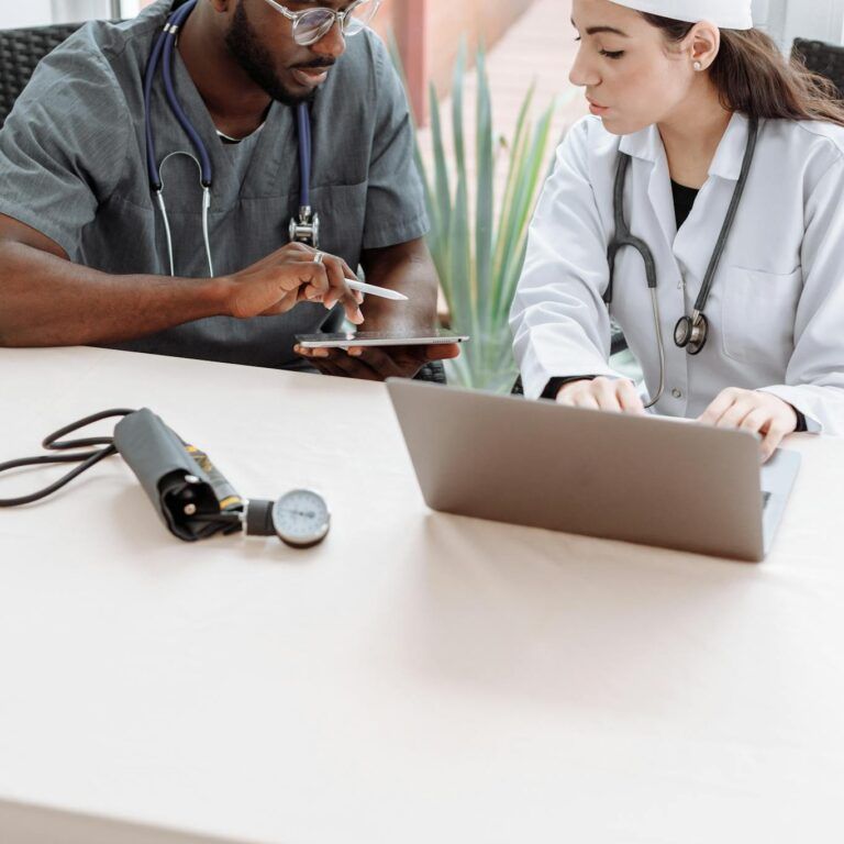 Medical Professionals Looking at the Screen of the Tablet while Sitting Next to Each Other